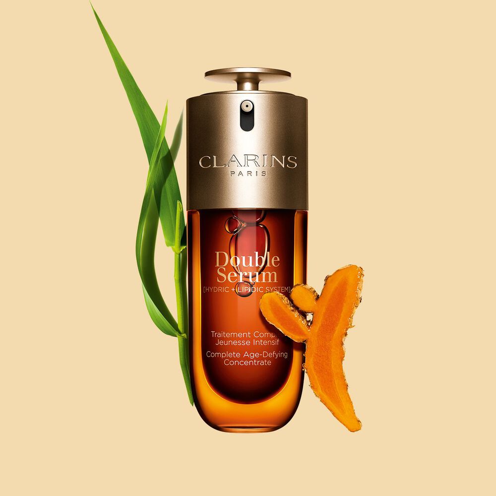 Abbildung von Clarins Double Serum vor den Hauptinhaltsstoffen Curcuma und Pfahlrohr auf einem goldenen Hintergrund