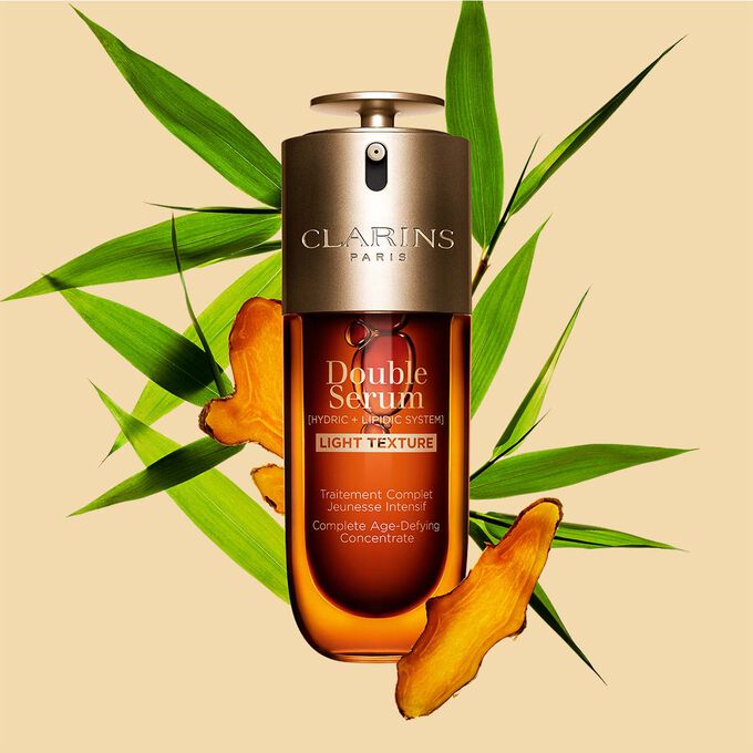 Ein 50ml Flakon Clarins Double Serum Light Texture zwischen Curcuma und Pfahlrohr auf orangefarbenen Hintergrund