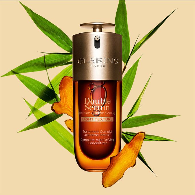 Ein 75ml Flakon Clarins Double Serum Light Texture zwischen Curcuma und Pfahlrohr auf orangefarbenen Hintergrund